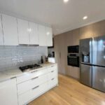 Scandi style kitchen with white cabinets, stainless steel appliances, light wood flooring, and a minimalist design.